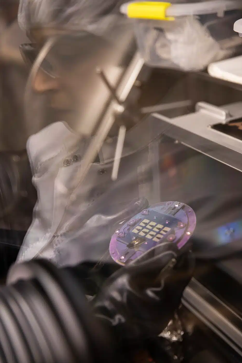 A worker is utilizing microscopy to work on a chip in a nano sciences factory.