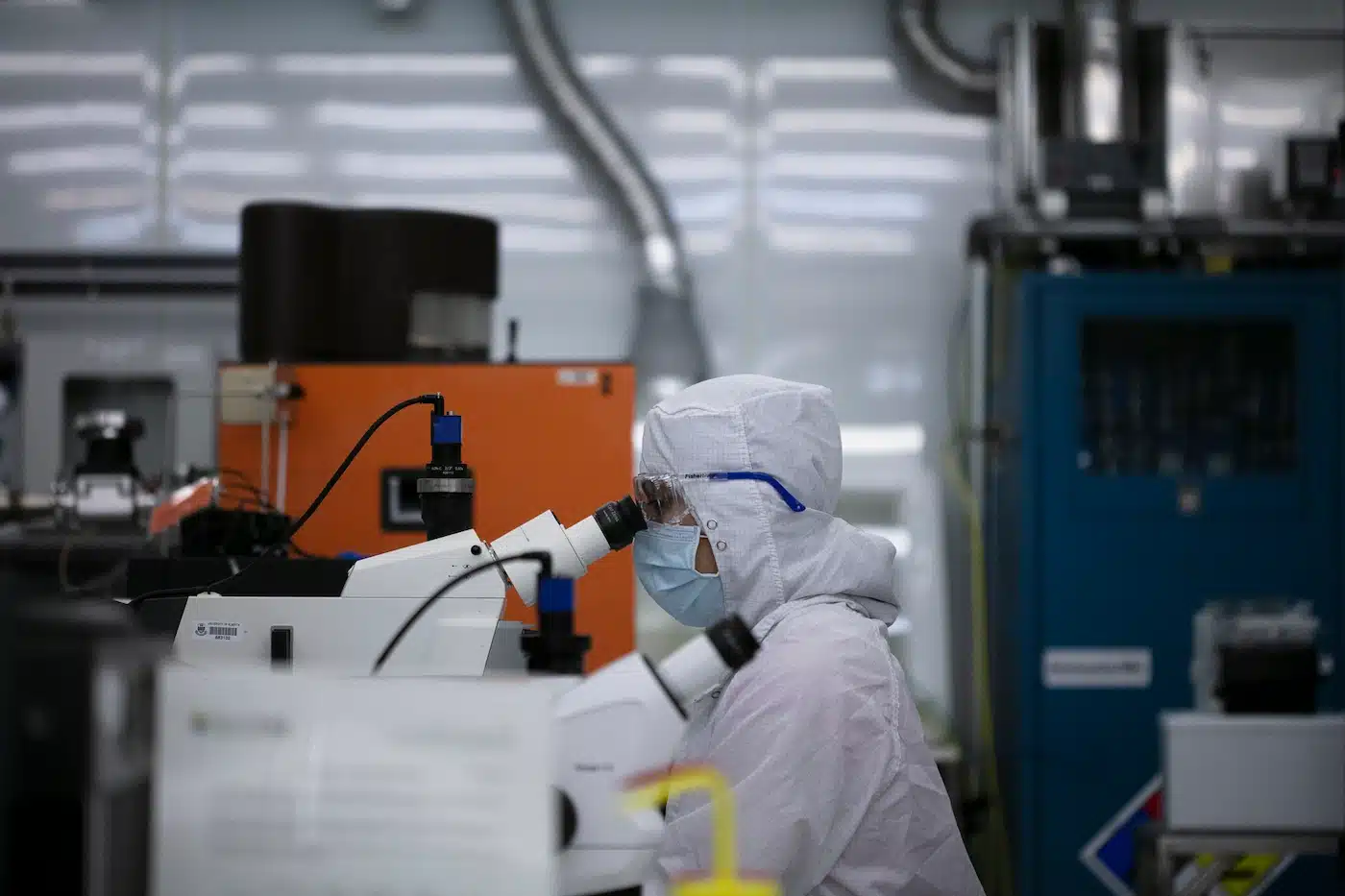 A worker using a microscope for nanofabrication research in a lab.